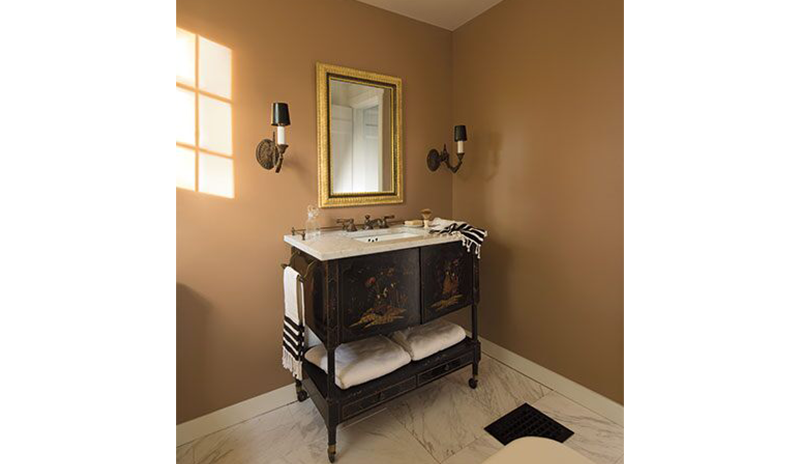A light orange-painted bathroom with classic sink, gold mirrors, and two wall lights.