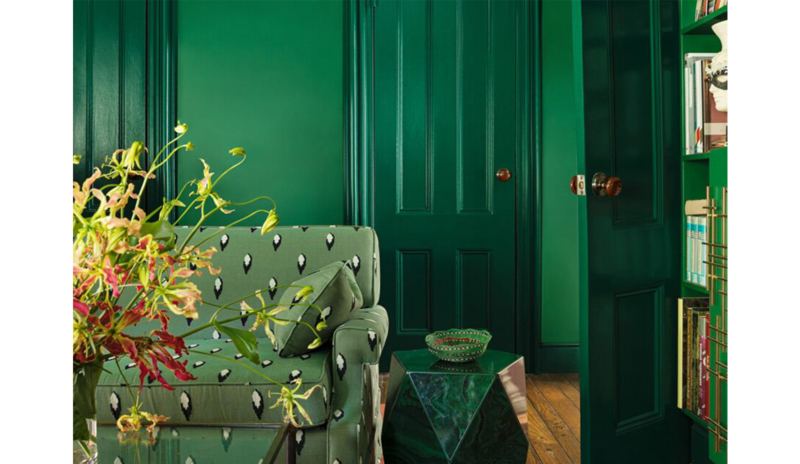 Green living room with matching walls, printed couch, stone table, glass coffee table, and bookshelv