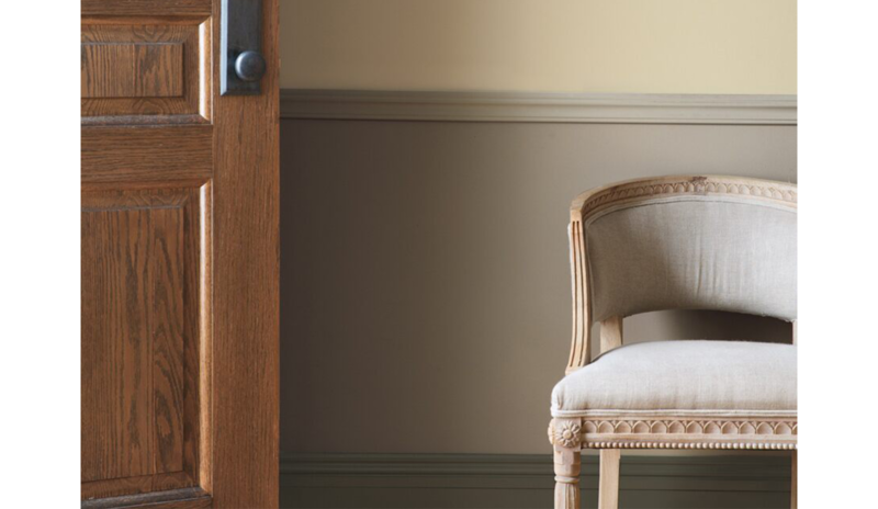Taupe entryway with wooden door, wainscoting, and beige chair.