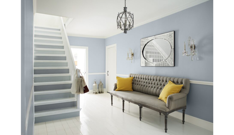 Blue-gray living with two-toned stairs, wainscoting, gray couch, yellow pillows, cage chandelier