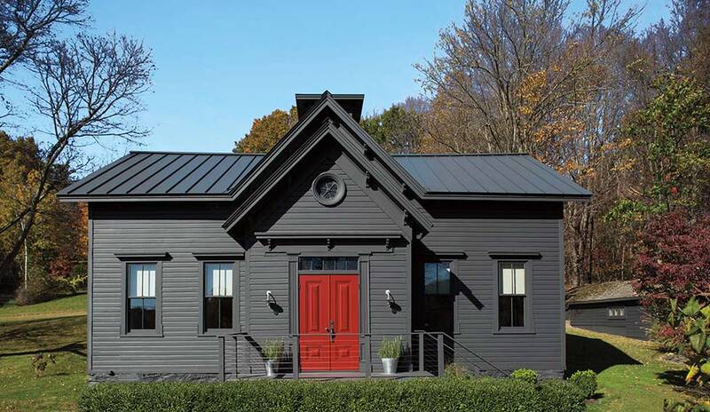 A dark gray-painted house with a bright red front door, a front hedge and autumn foliage.