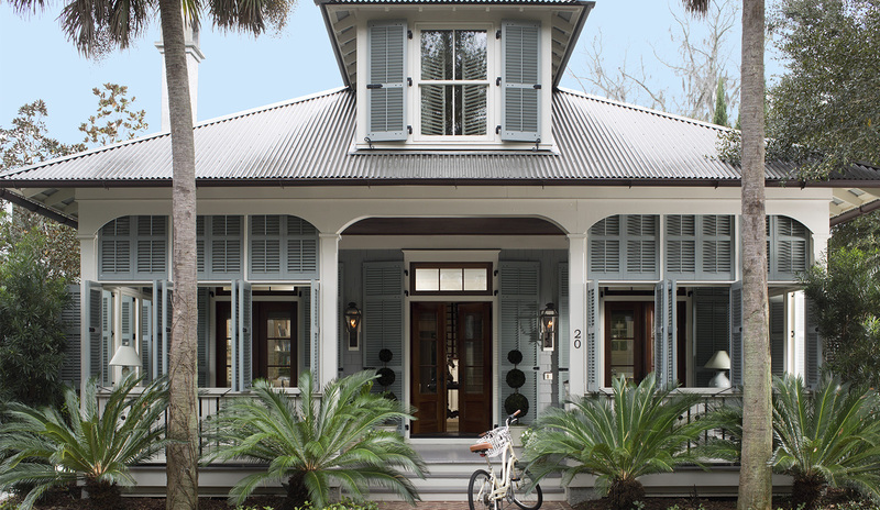 Light blue Key West-style home with front porch in tropical landscape.