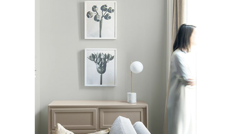 Light gray living room with two picture frames hanging above a wood cabinet next to a gray sofa. Light gray living room with two picture frames hanging above a wood cabinet next to a gray sofa.