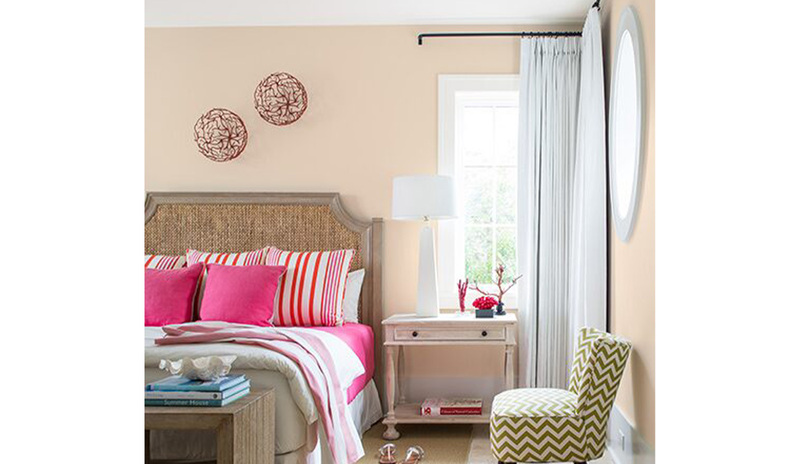 Peach-painted bedroom walls with a green chevron chair, side table, and bed featuring pink bedding. Peach-painted bedroom walls with a green chevron chair, side table, and bed featuring pink bedding.