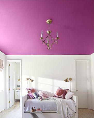 White bedroom: white bed and bedding, multicolored pillows, geometrical end table, books, dog White bedroom: white bed and bedding, multicolored pillows, geometrical end table, books, dog