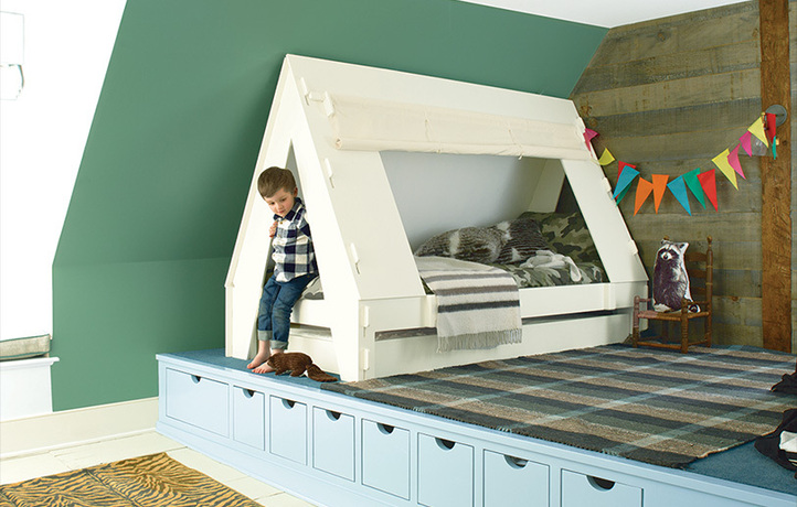 A green-painted angled wall frames a platform with a little boy and his tent bed. A green-painted angled wall frames a platform with a little boy and his tent bed.