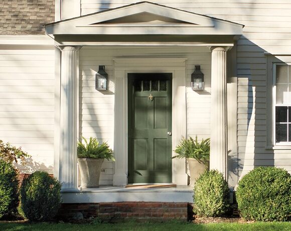 A pretty covered entrance of a white-painted house with a dark green front door, two white columns