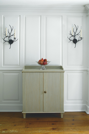 Panelled gray-painted walls frame a chest centered between candle sconces. Panelled gray-painted walls frame a chest centered between candle sconces.