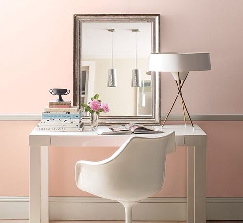 Two-toned pink-painted walls with a leaning mirror above a white desk and chair. Two-toned pink-painted walls with a leaning mirror above a white desk and chair.