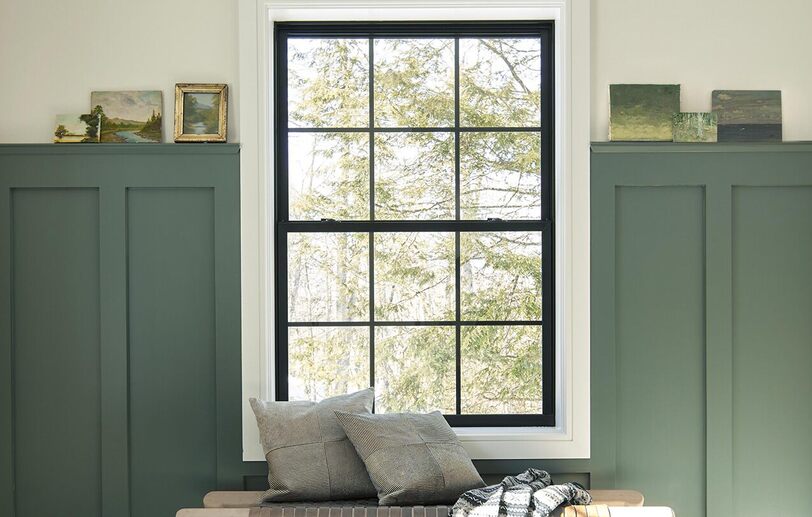 An inviting entryway with dark green-painted wainscoting, white walls and trim, a large window 