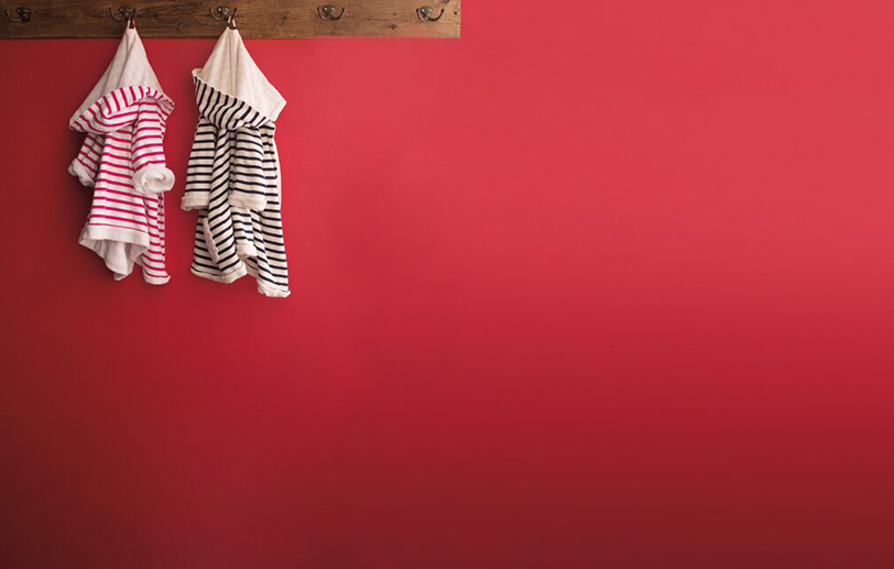 Red wall with a wooden plank coat rack, two striped children's robes, one in pink and one in black. Red wall with a wooden plank coat rack, two striped children's robes, one in pink and one in black.