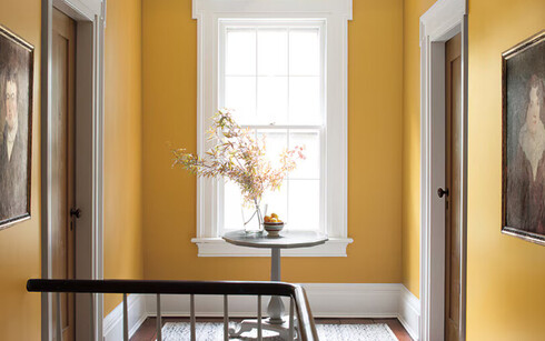 Yellow-painted hallway with wooden table and flowers, two doors, a window, and white-painted trim.