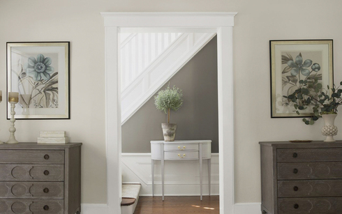 A gray and neutral hallway leads to a white staircase.