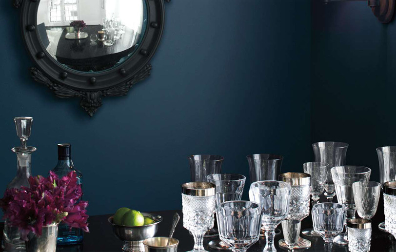 A dark blue-painted room with black framed mirror and crystal glasses on a table. A dark blue-painted room with black framed mirror and crystal glasses on a table.