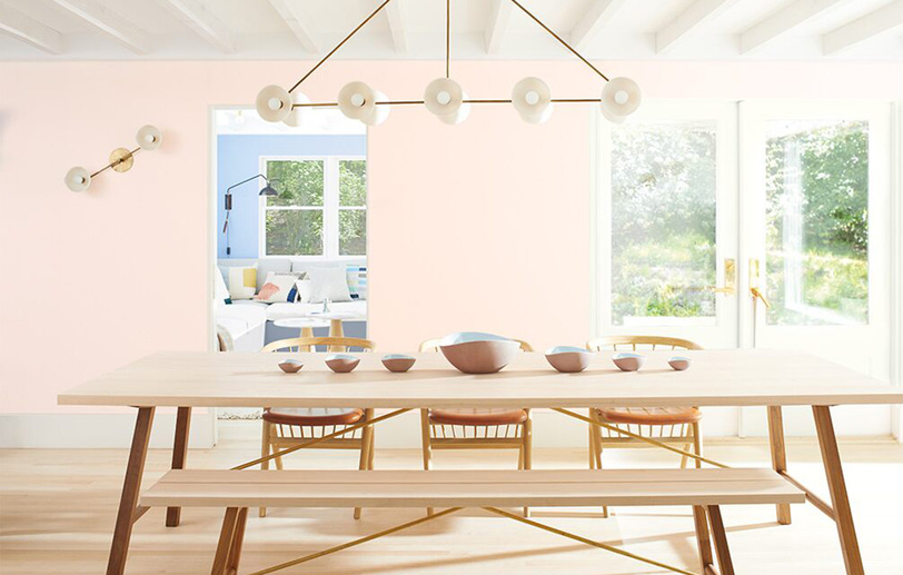Light pink-painted dining room walls with a long wooden table, matching chairs and bench seating. Light pink-painted dining room walls with a long wooden table, matching chairs and bench seating.