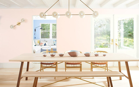 Light pink-painted dining room walls with a long wooden table, matching chairs and bench seating.